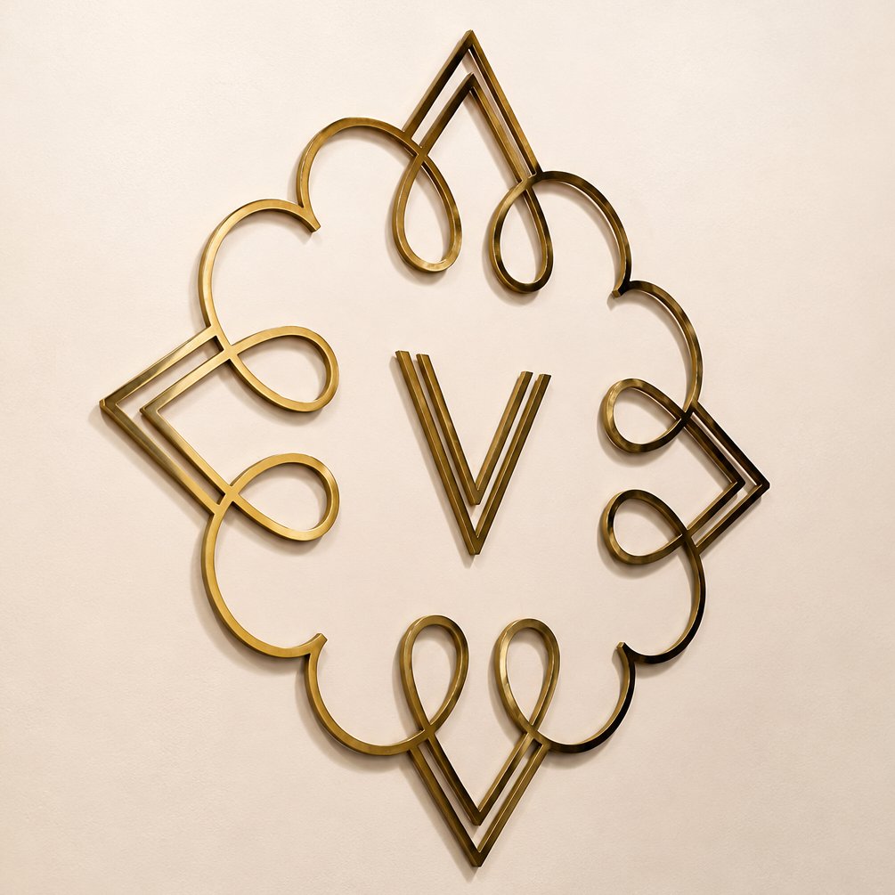 The Vicinity V monogram in polished gold on a cream wall